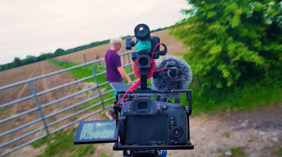 DSLR camera with cage and microphone being carried toward a gate and field