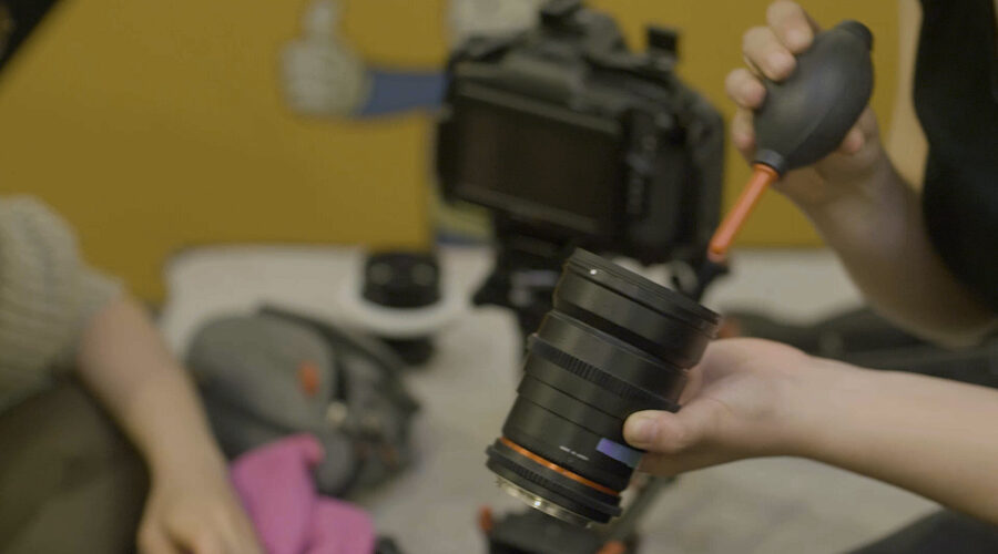 hands cleaning a camera lens with a duster