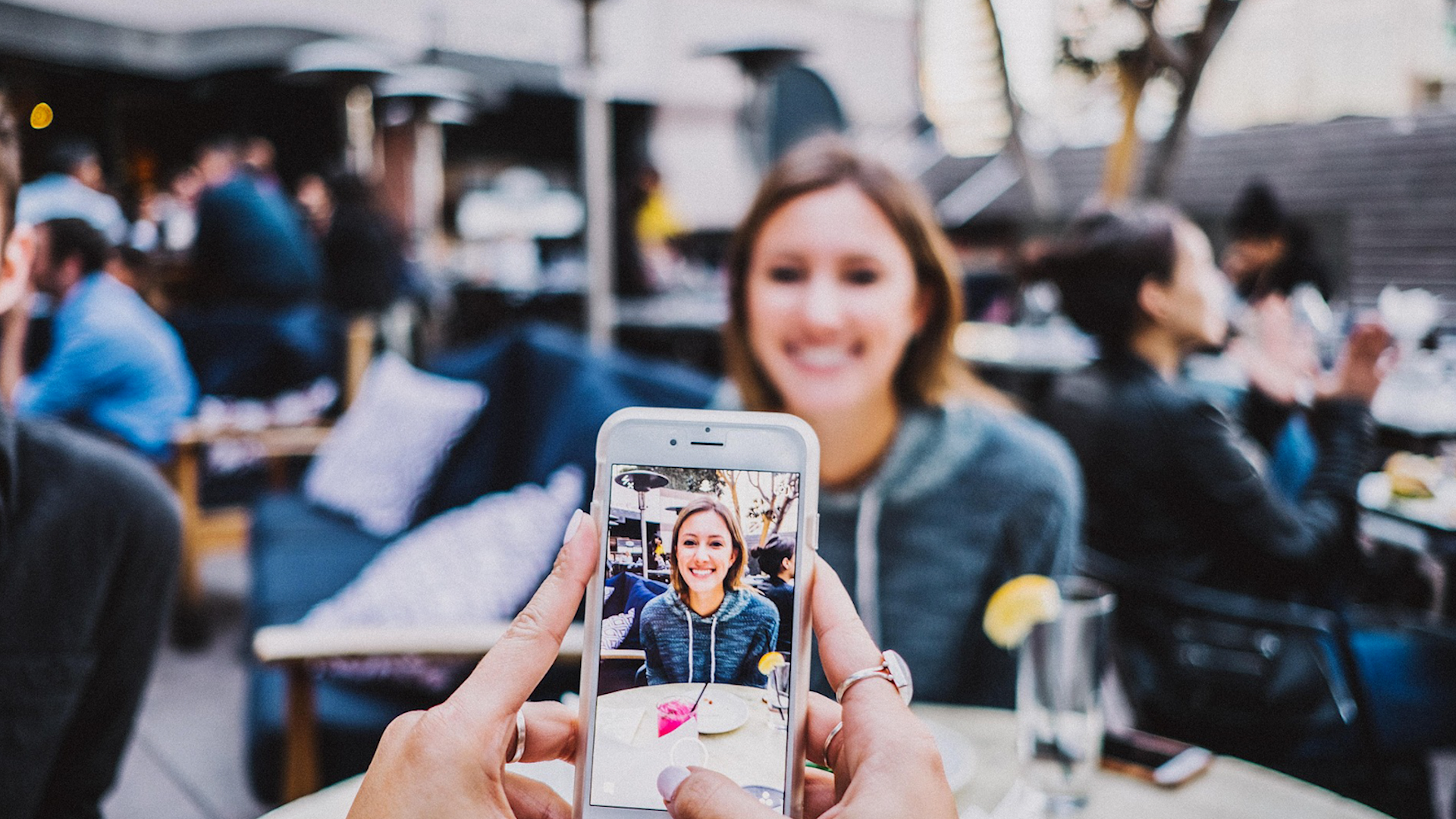 iphone taking a photo of a woman sitting at a cafe table outdoors