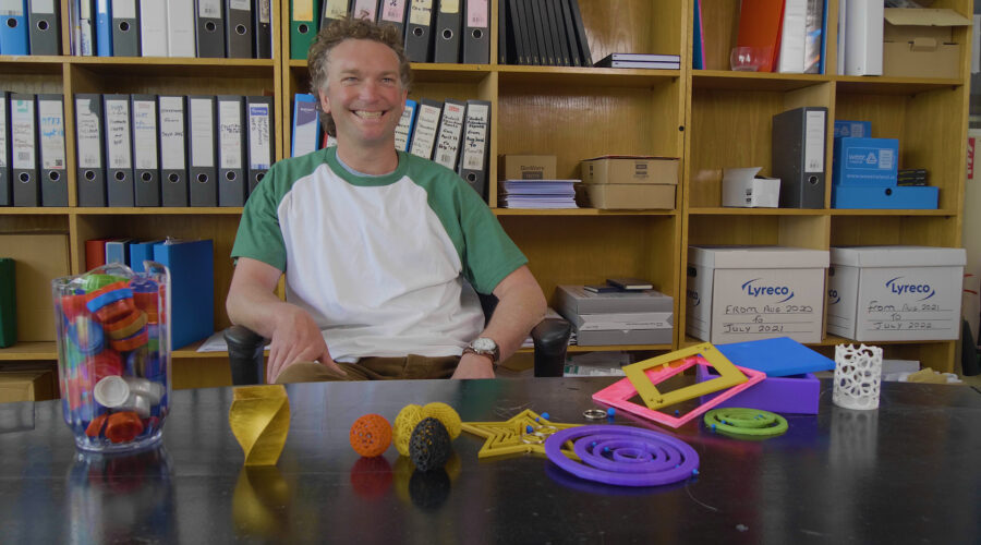 Man sitting at an office desk giving an interview to camera