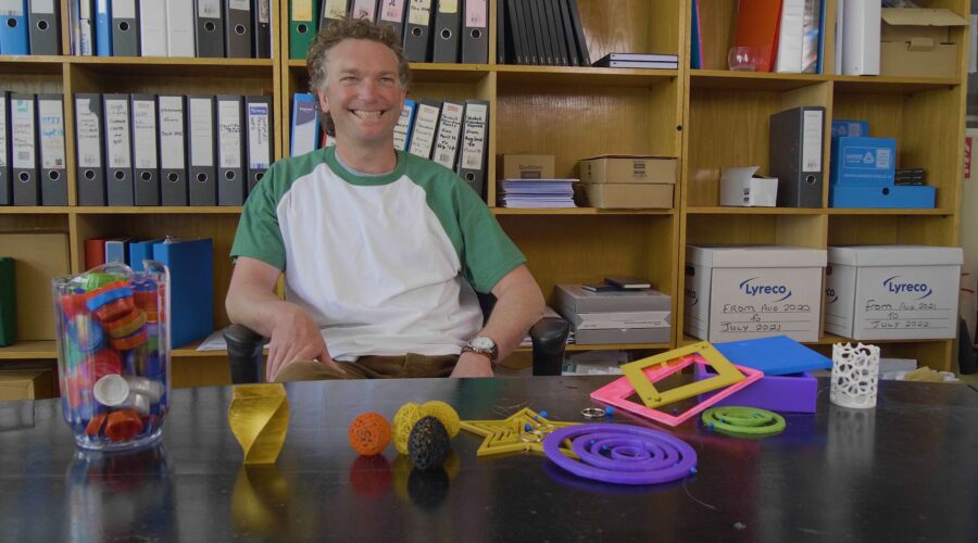 man sitting behind a desk being interviewed on camera